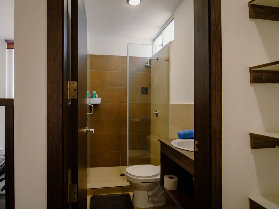El segundo baño de CASA A12, con ducha y repisas de madera.