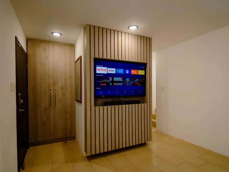 El televisor de CASA A12 sobre un panel de listones de madera, junto a la puerta de entrada.