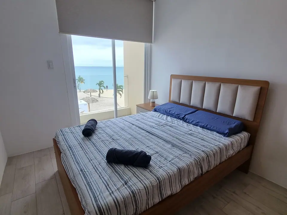 Un dormitorio con cama doble de sábanas a rayas y ventana hacia el mar.