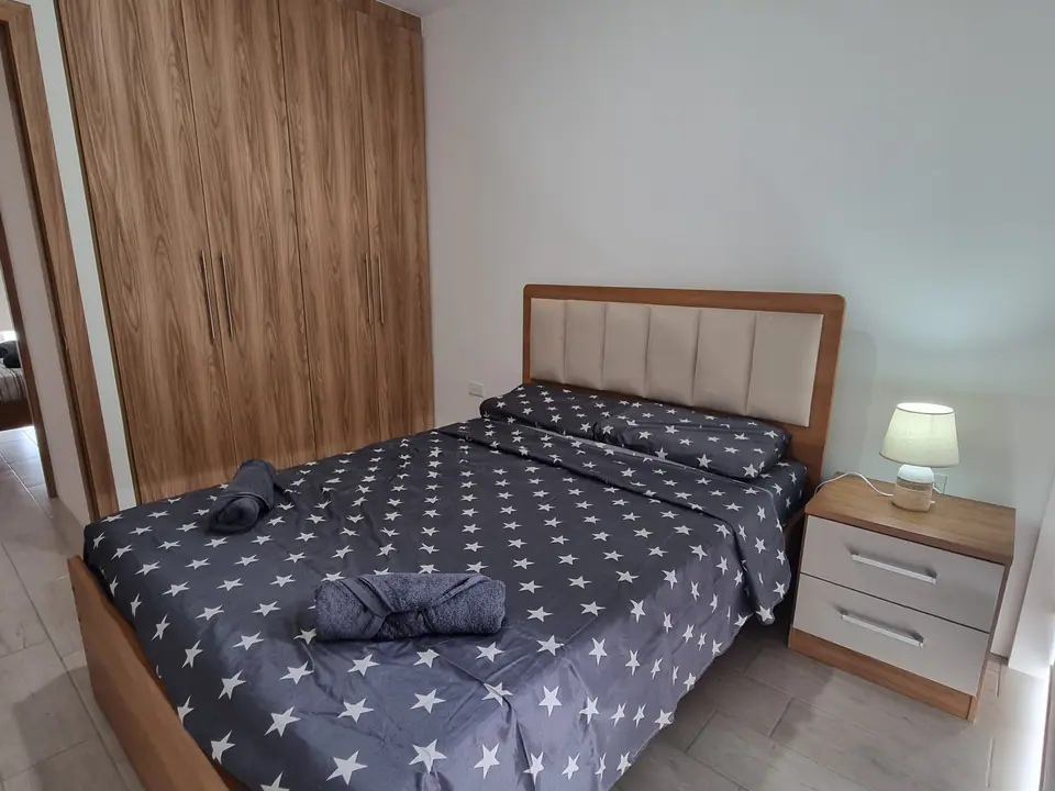 Un dormitorio con cama doble, mesa de noche con lámpara y un panel de madera en la pared.
