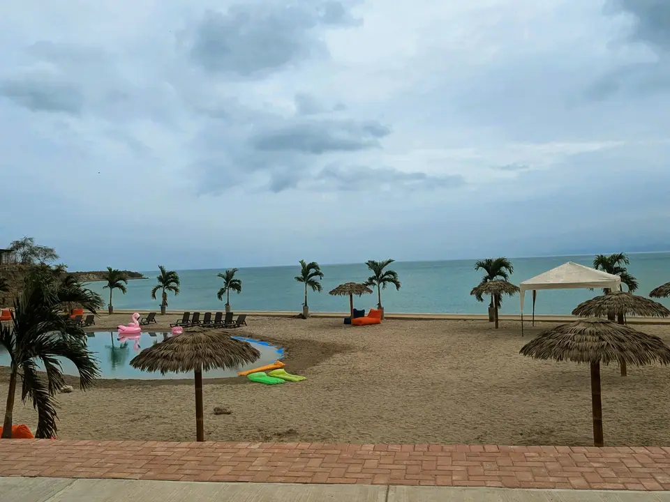 El club de playa de Punta Arrecife: una laguna con arena, palmeras y sombrillas de paja, y el mar detrás.