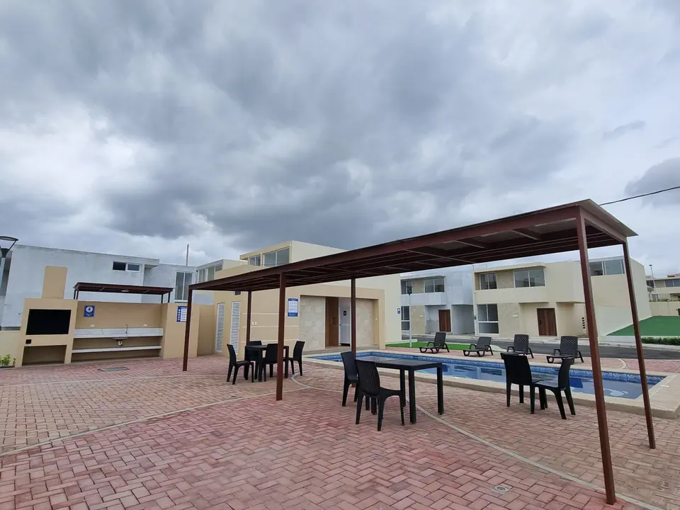 La zona social junto a la piscina: una pérgola con mesas y sillas y una parrilla de obra.