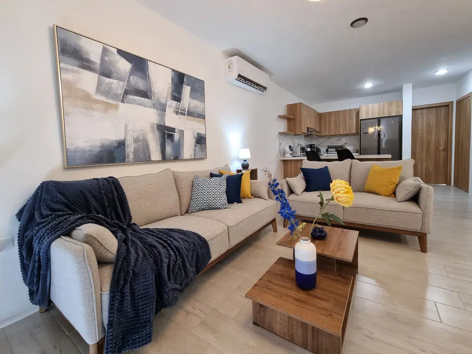 Los dos sofás de la sala con la mesa de centro de madera; al fondo, la cocina.