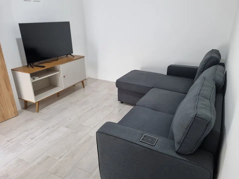 El cuarto con sofá cama gris y televisor sobre un mueble blanco.