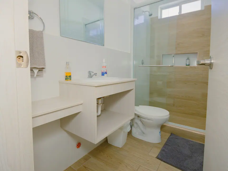 Baño de CASA C5 con lavamanos, mueble claro y ducha revestida en madera.