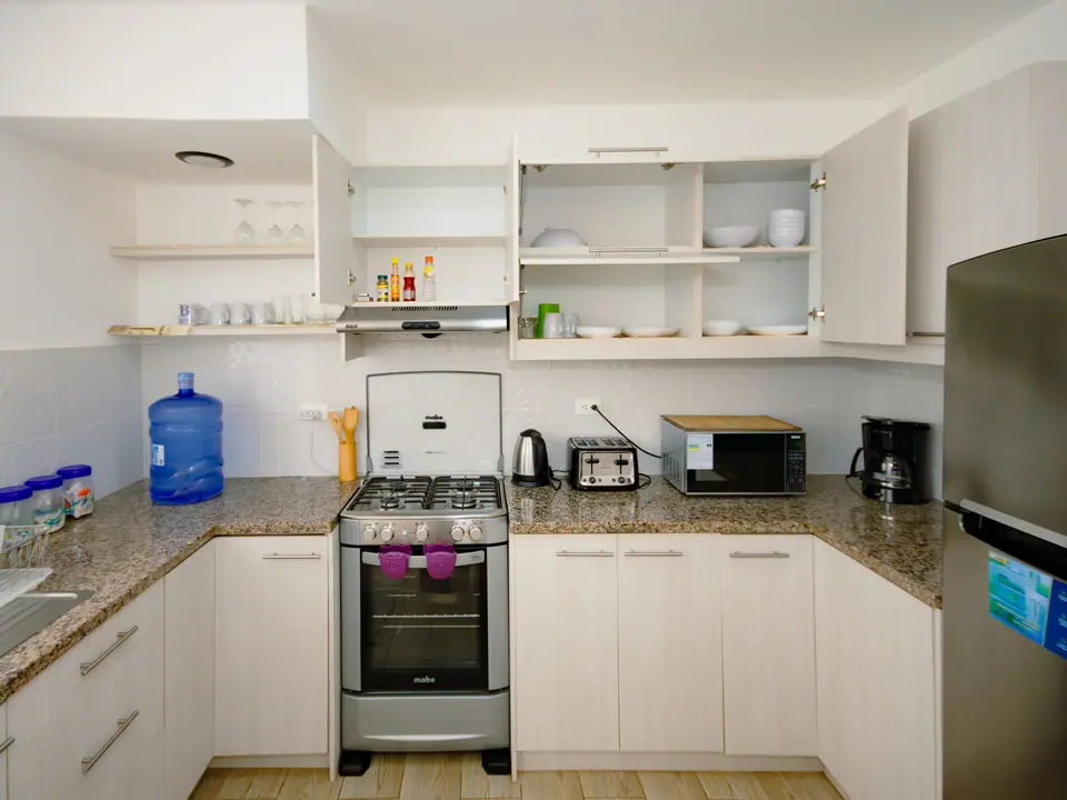 La cocina de CASA C5 con las alacenas abiertas: vajilla, vasos, tostadora, microondas y cafetera.