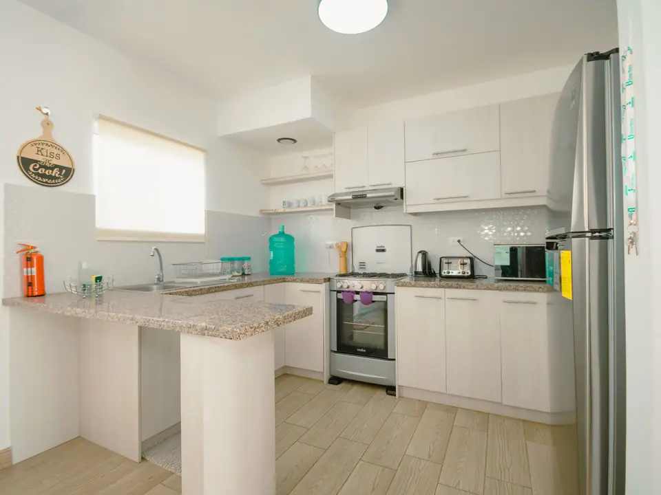 La cocina de CASA C5: muebles claros, mesón de granito, cocina a gas con horno y refrigeradora.