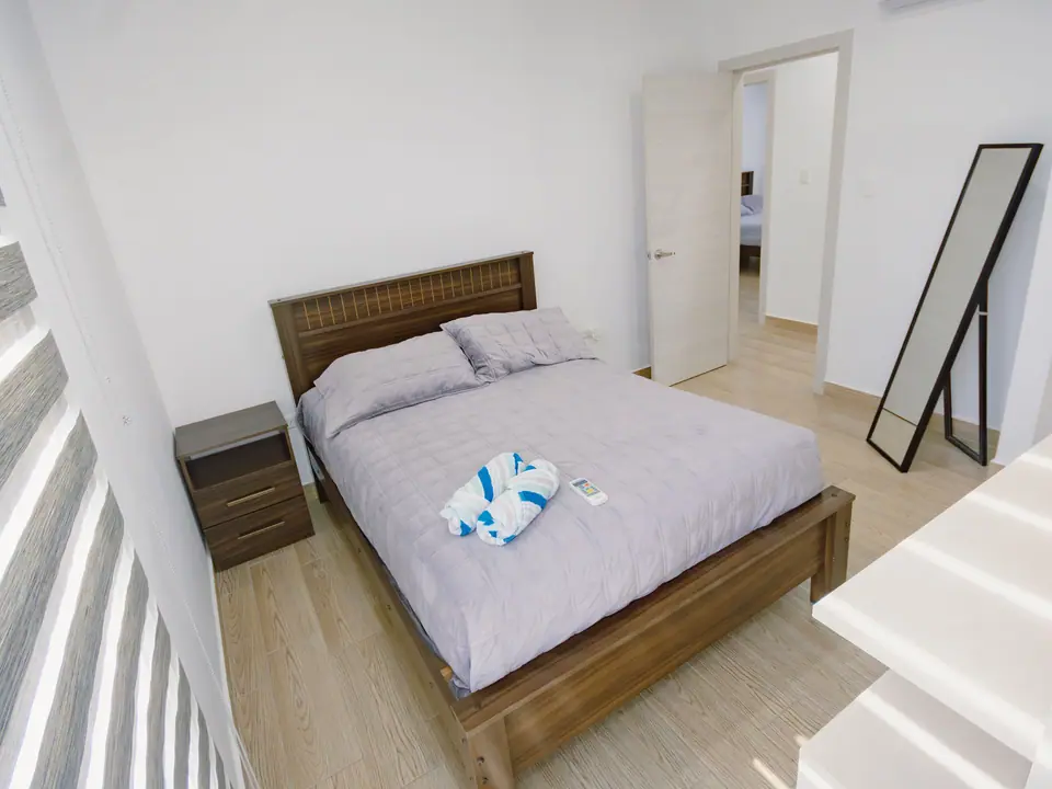 El dormitorio principal de CASA C5, con cama doble, espejo de pie y la puerta al pasillo.