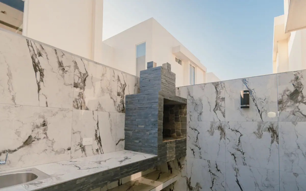 El patio de CASA A12, revestido de porcelanato, con la parrilla de carbón al fondo.
