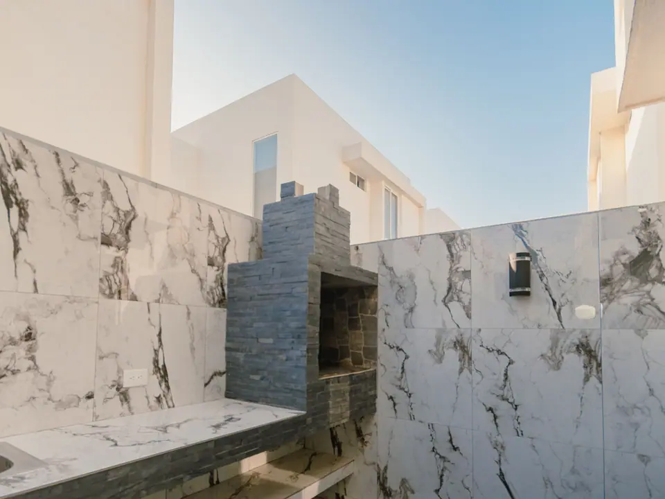 El patio de CASA A12, revestido de porcelanato, con la parrilla de carbón al fondo.