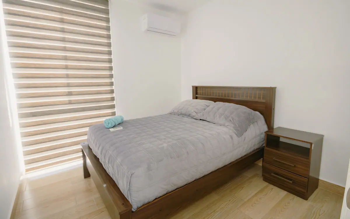 Dormitorio de CASA C5: cama doble, aire acondicionado sobre la ventana y persianas enrollables.