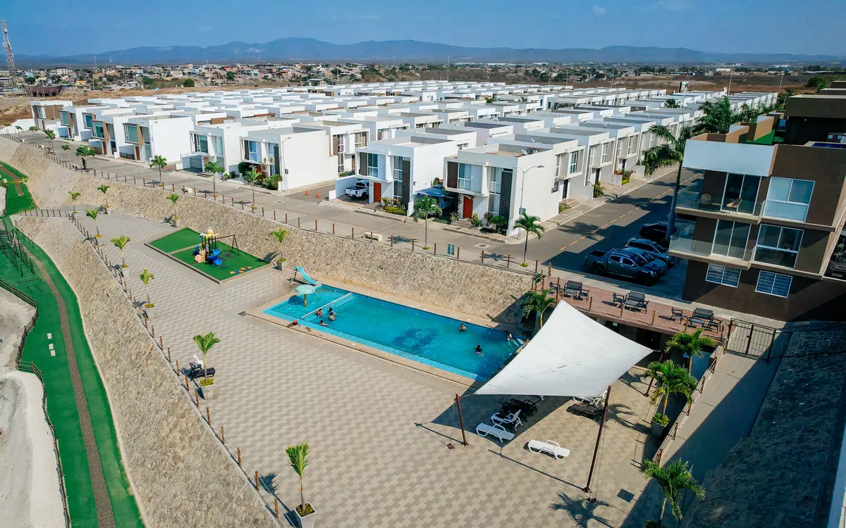 La piscina de la urbanización vista desde arriba, con el toldo blanco y el área de juegos junto al acantilado.
