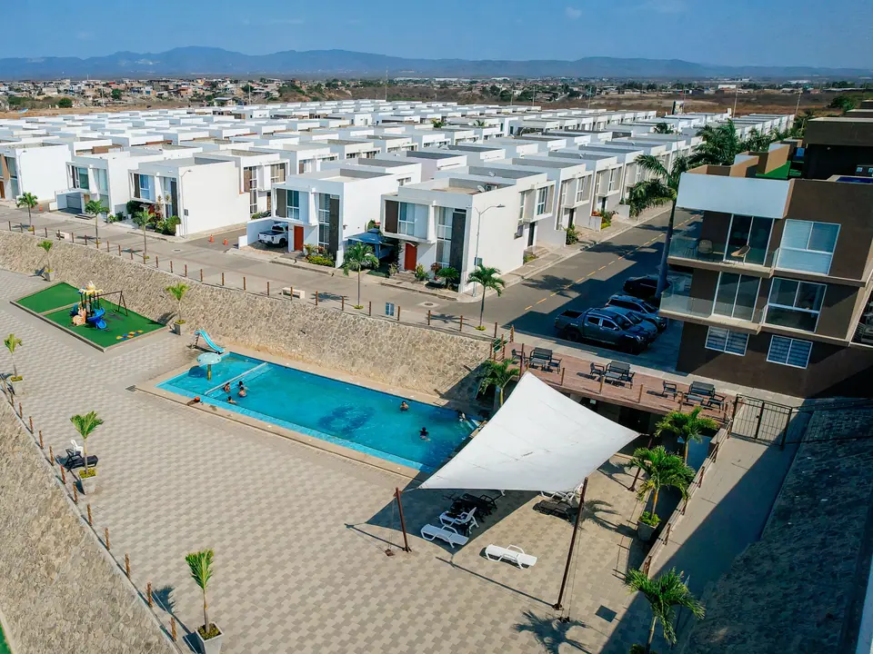 La piscina de la urbanización vista desde arriba, con el toldo blanco y el área de juegos junto al acantilado.
