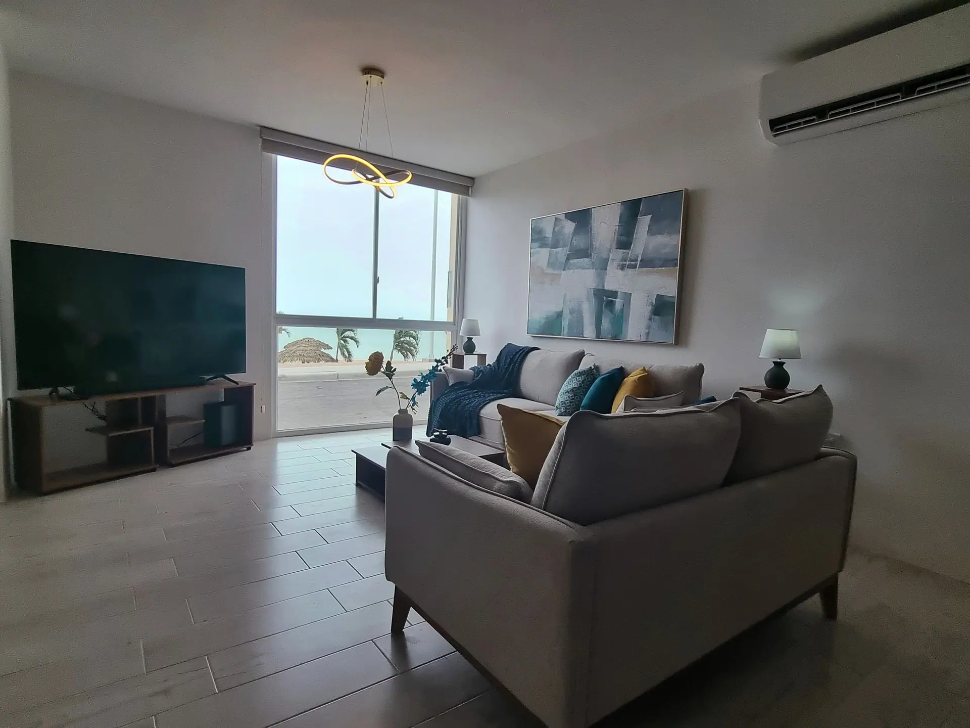 La sala de Punta Arrecife: sofás claros, un televisor grande y un ventanal por el que se ve el mar.
